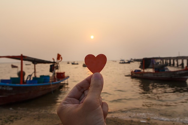 Close up of hand man holding a paper heart with the sea background in evening. love concept, happy valentine.