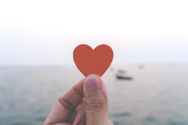 Close up of hand man holding a paper heart with the sea background. love concept, happy valentine.