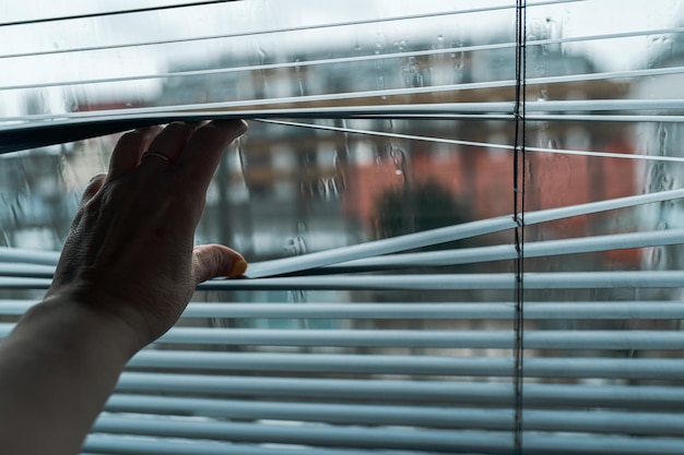 Close up hand opens jalousie against through window