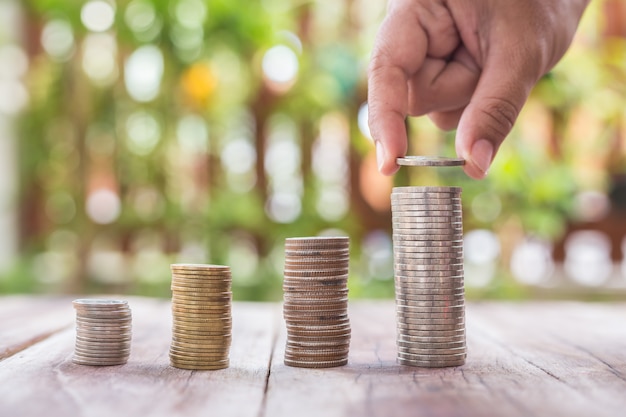 Close up hand putting coins in stack on wooden plank. savings concept.