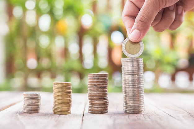 Close up hand putting coins in stack on wooden plank. savings concept.