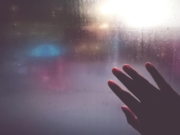 Close-up of hand touching wet window