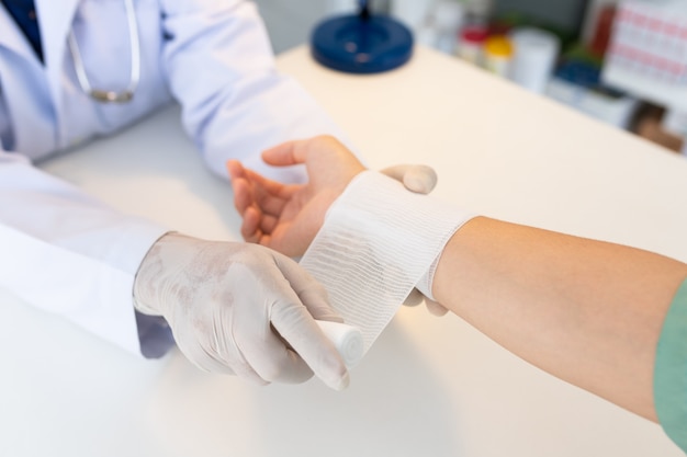 Photo close-up hand wear medical gloves  of doctor hand tying bandage on the hand of patient in clinic, osteophytes and heel, fascia