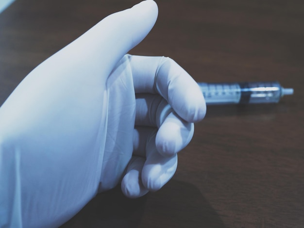 Photo close-up of hand wearing surgical glove while holding syringe