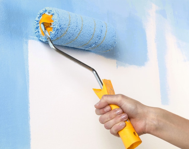 Close-up of a Hand with paint roller painting a blue wall