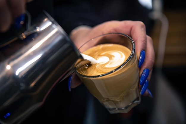 Close up hand of a woman barista pouring froth milk in espresso coffee