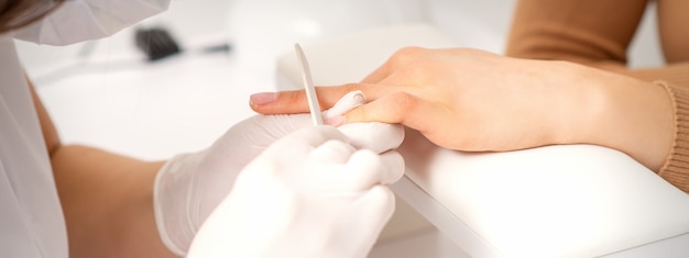 Close up of the hand of young woman receiving the nail file procedure in a beauty salon