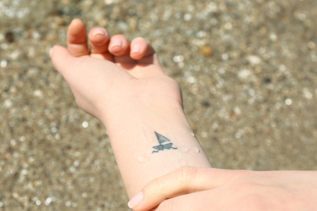 Close up of hand of young woman with ship tattooed in it on sea background