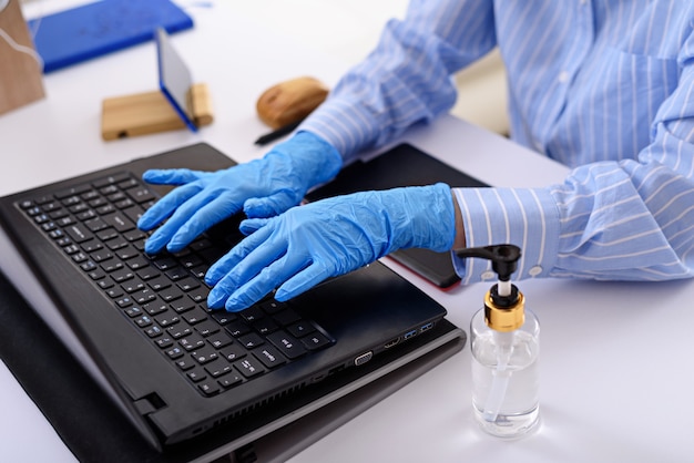 Close-up of hands in blue medical gloves typing on laptop, remote work at home, freelancer in quarantine concept