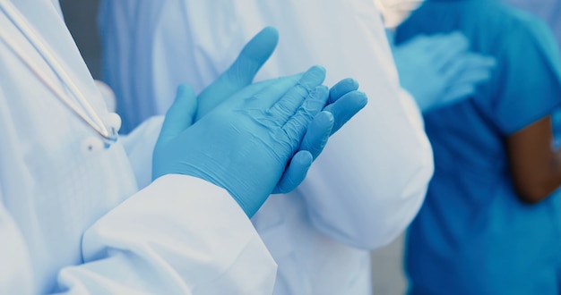 Close up of hands in blue rubber gloves applauding. Mixed-races males and females doctors. in white medical gowns. Applause. Multi ethnic medics. Physicians colleagues.