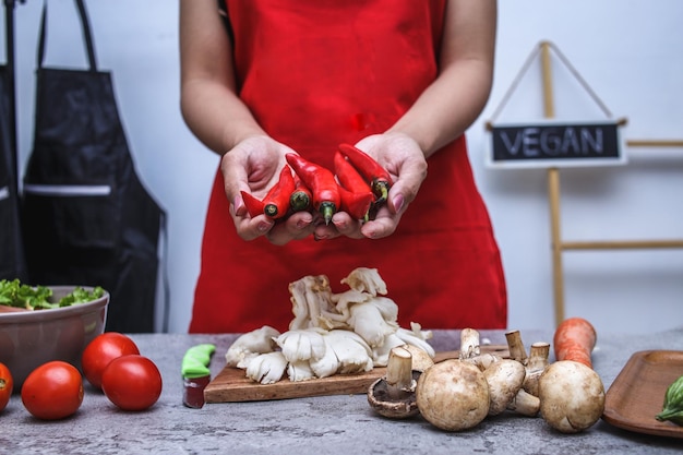 Close-up of hands of chef using apron holding red chili with various fresh food on the table.