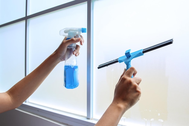 Photo close up hands cleaning window with bottle spray and blue squeegee cleaning service and housekeepin