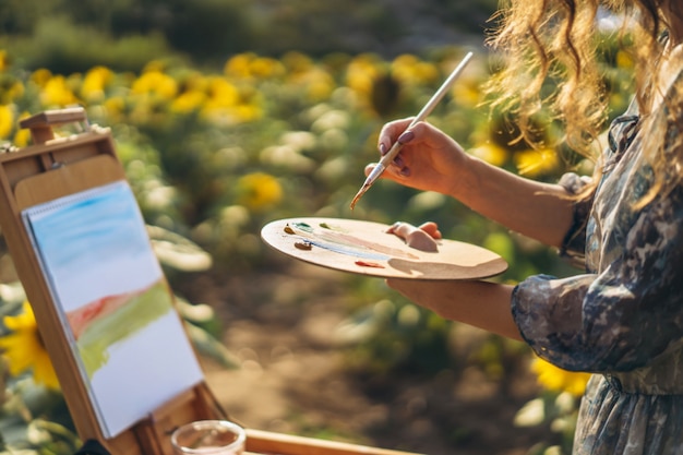 Close up hands of female artist holding brush and palette with oil paints.