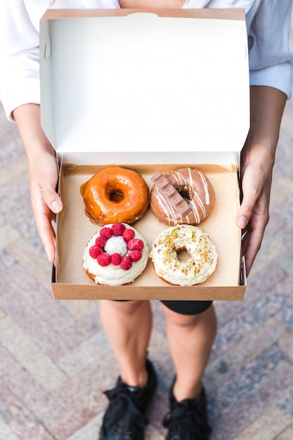 Close up hands holding four pieces of totally different colorful and delicious looking donuts in ecological carton box.