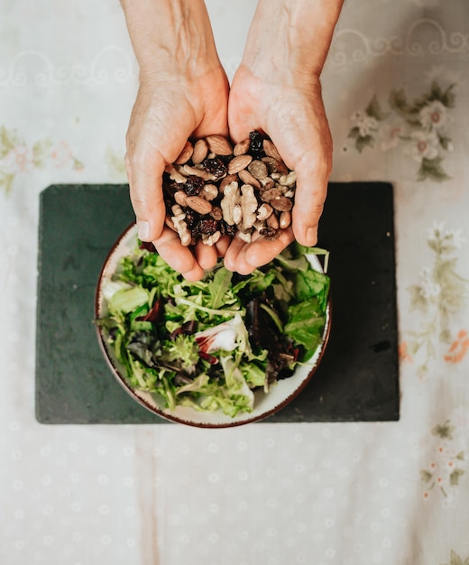 Close up of hands holding up several nutswalnutraisin and almond above a salad bowl with lettuceFinishing a vegan meal with nutrientscalories and proteins providing enough energy supply