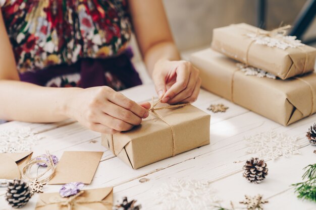 Close up of hands holding wrapping gift box on wooden table with xmas decoration.