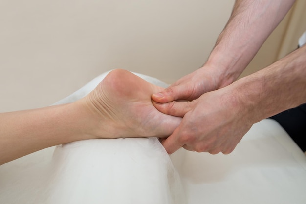 Close-up of hands of masseur doing foot massage to young girl in massage parlor.