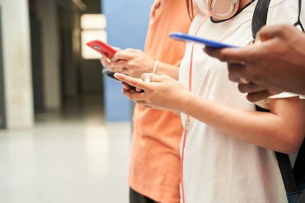 Close up of the hands of a multiethnic group of unrecognizable students using a smart phone connecte...