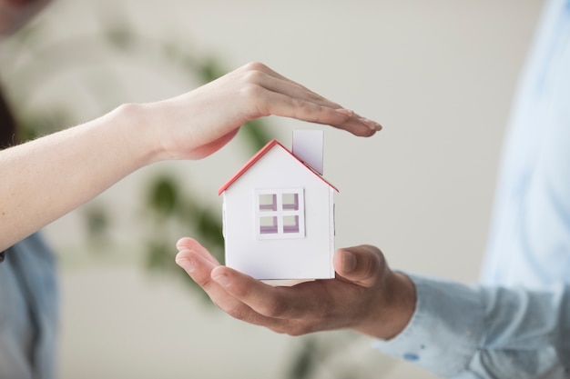 Close-up of hands protecting small house model