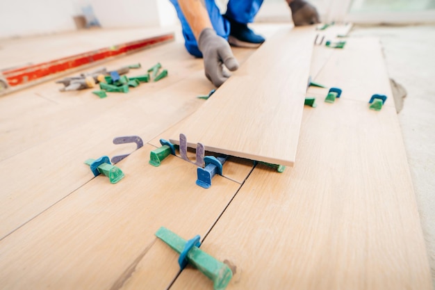 Close up hands of repairman laying tiles with tile leveling system on the floor in a new house