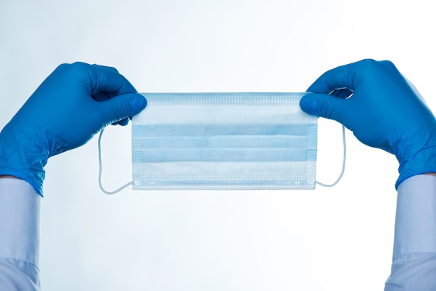 Close up of hands in rubber gloves holding a surgical mask. Isolated on white background. COVID 19 Coronavirus