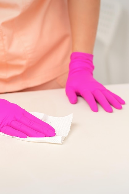 Close up of hands in rubber protective pink gloves cleaning the white surface with a white rag.