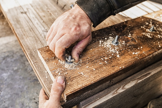 Close up of hands screwing a bolt into a wooden board