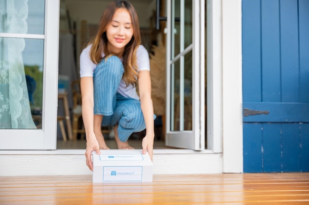 Close up hands of sick Asian woman sitting at door to receive medication first aid pharmacy box package from hospital delivery service at floor home, drugstore internet online medical business