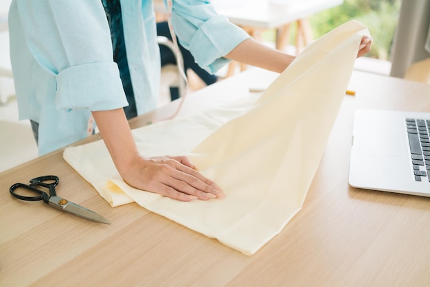 Close up hands of a tailor or fashion designer touch stretch and feel the texture of linen fabric with a laptop on the table Checking for new material for a new collection of clothes at the atelier