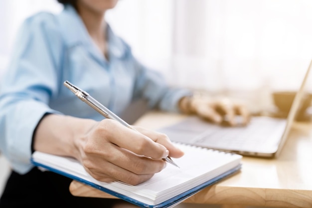 Close-up of hands Taking written Notes to on notebook and freelance business female casual working with laptop computer ,warm milk cup in coffee shop like,Distance job communication concept