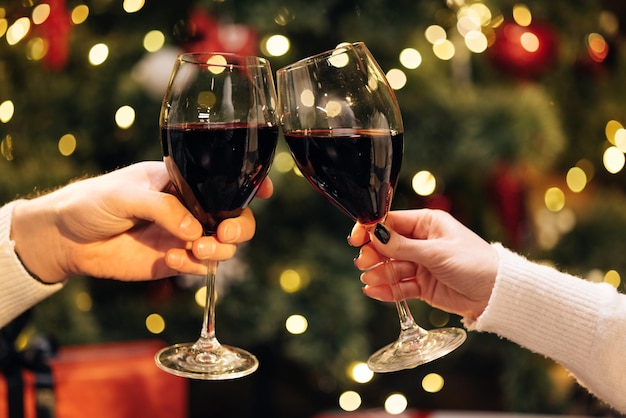 Close up hands of unknown people who cheering with glasses of wine against christmas tree decorated