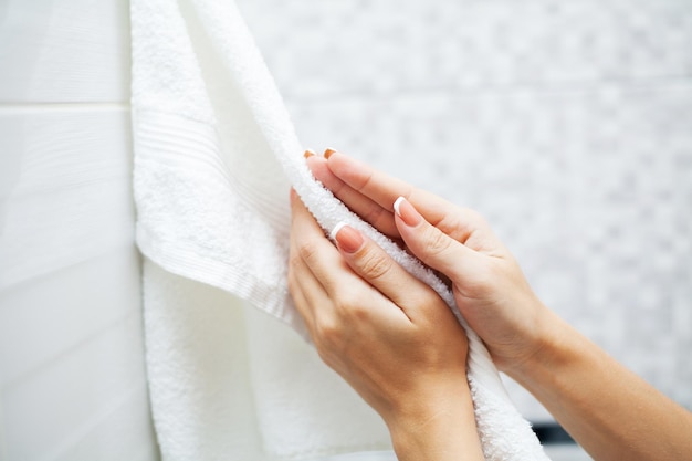 Close up hands use white towel in light bathroom.