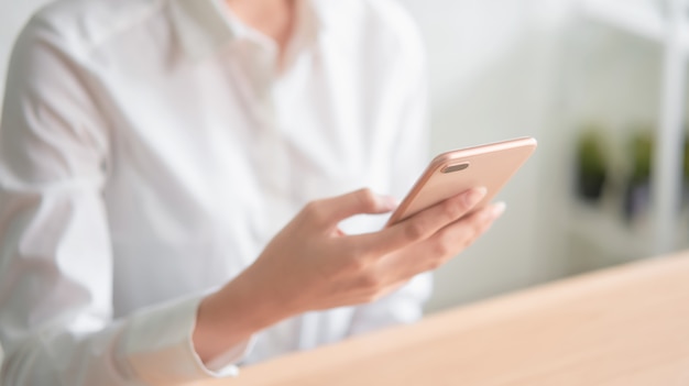 Close-up of hands using smartphone on wooden table and typing message to his friends.