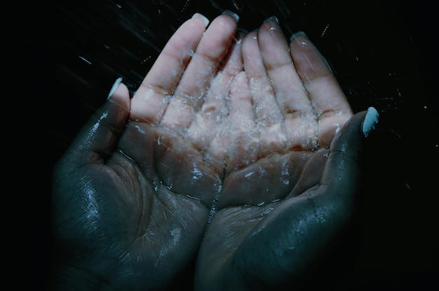 Close up of hands with water against black background