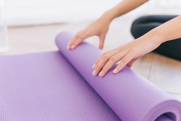 Close up hands of woman rolling yoga mat preparing for doing yoga Working out at home or in yoga studio Healthy habits keep fit weight loss concepts