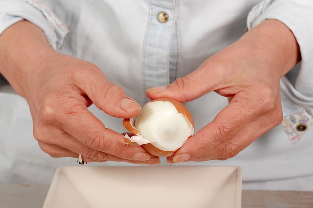 Close up of hands of woman shells hard-boiled egg