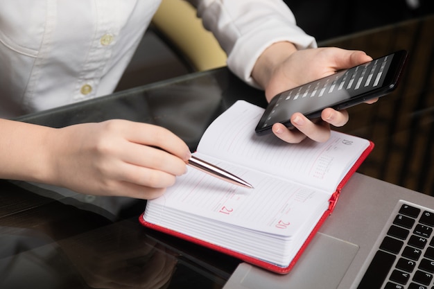 Close-up Of the hands of Young businesswoman holding mobile phone and make notes in diary