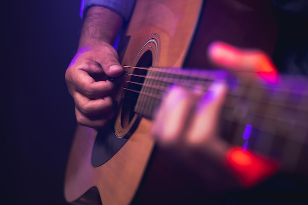 Close up hands young man playing acoustic guitar on stage live in concert. With neon light. Young man practicing music and solo guitar on the show.