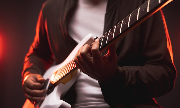 Close up hands young man rocker playing electric guitar on stage live in concert. With neon light. Young man practicing heavy metal music and solo guitar on the show.