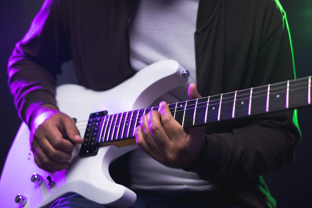 Close up hands young man rocker playing electric guitar on stage live in concert. With neon light. Young man practicing heavy metal music and solo guitar on the show.