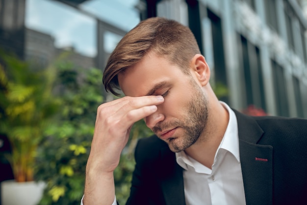 Close up handsome young businessman in black suit looking tired