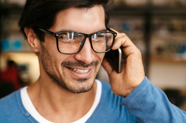 Close up of a handsome young man wearing glasses at the library, talking on mobile phone