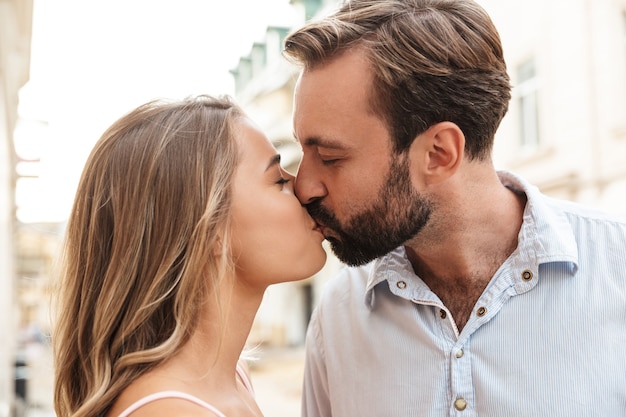 Close up of a happy beautiful couple embracing while standing at the city street, kissing