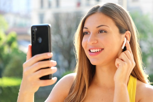 Close up of happy girl choosing music on her smart phone with wireless earphones outdoor in summer sunny day