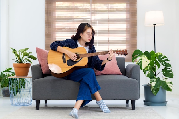 Close up happy glasses Asian girl playing acoustic guitar in living room at home Recreation at home concept