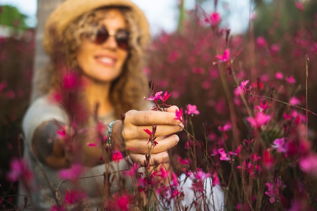 Close up of happy woman touching pink flower in spring meadow outdoor leisure activity Welcome spring season Concept of cheerful female in background defocused and nature in foreground