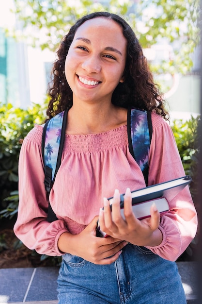 Close up happy young latin student woman holding her books outside the campus. Education concept