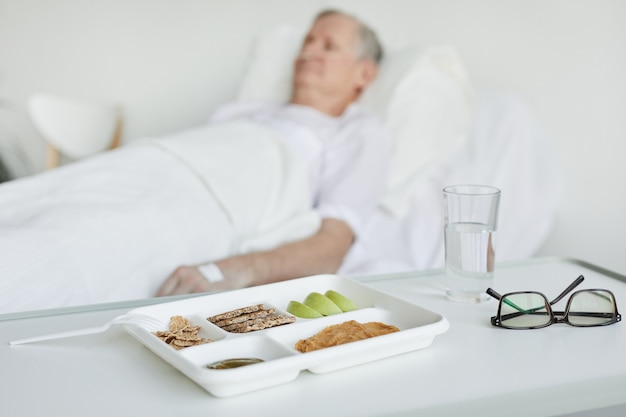 Close up of healthy hospital food on tray with patient in background, copy space