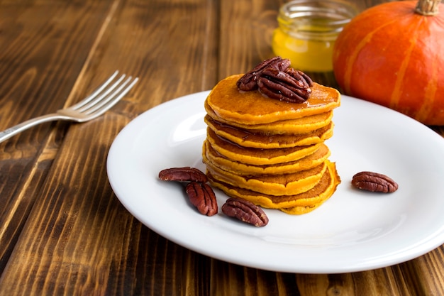 Close-up on homemade pumpkin pancakes with honey and pecans in the white plate on the rustic background