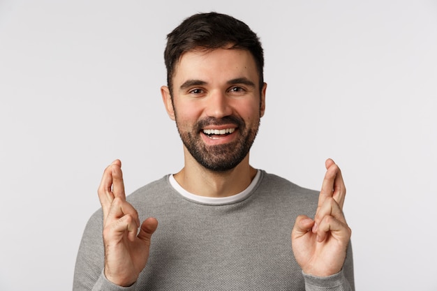 Close-up hopeful and cheerful, optimistic bearded adult guy in grey sweater, believe miracle happen, hope dream come true, cross fingers good luck, praying or relish deal went well